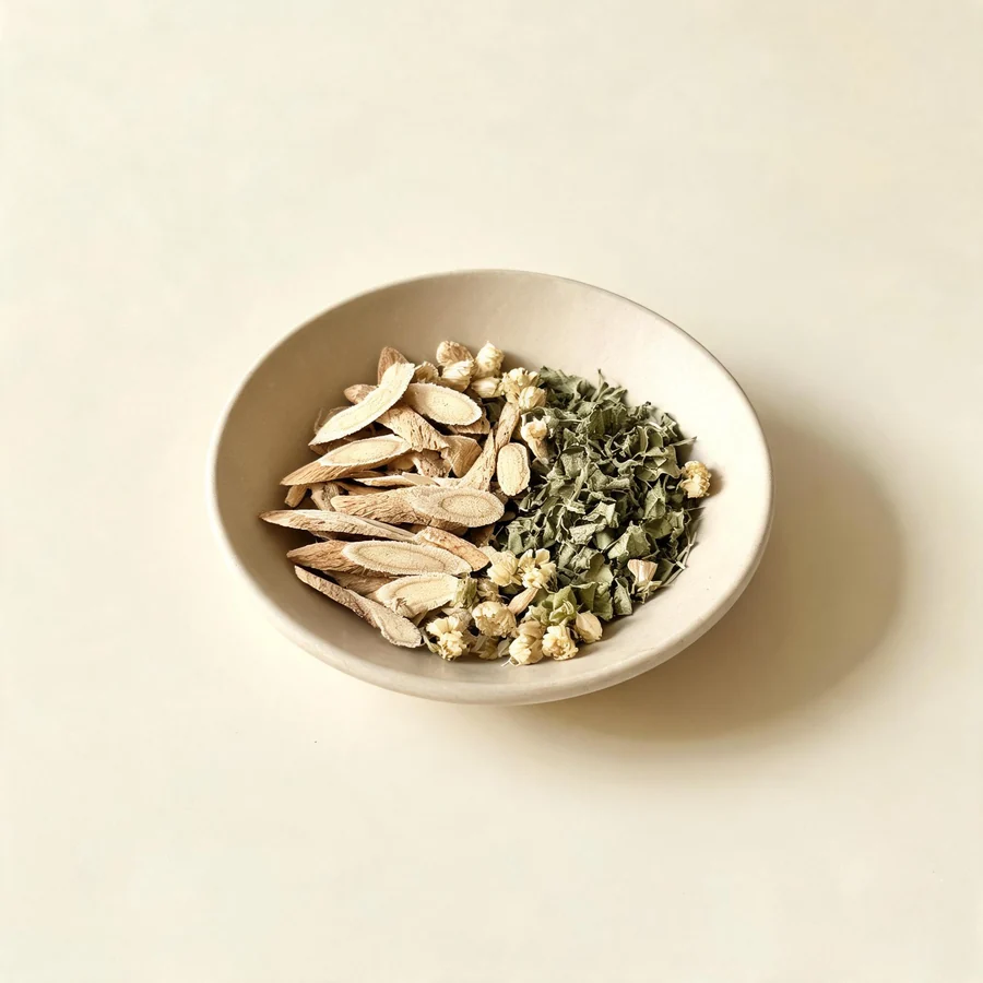 An editorial still life of the traditional Chinese herbs used for this condition, arranged on a warm off-white surface: pale root slices.