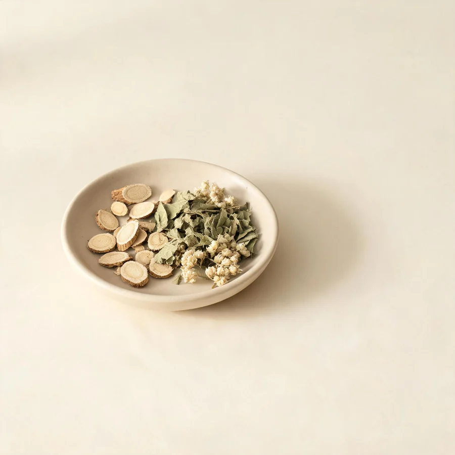 An editorial still life of the traditional Chinese herbs used for this condition, arranged on a warm off-white surface: pale root slices.