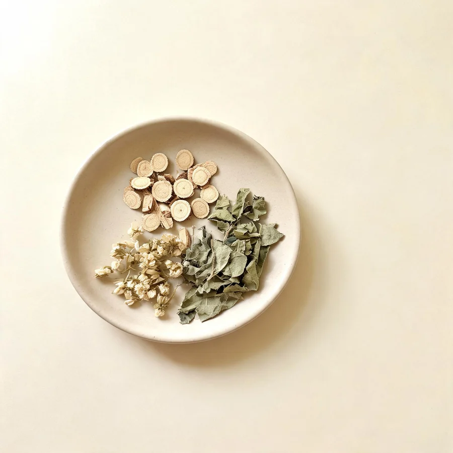 An editorial still life of the traditional Chinese herbs used for this condition, arranged on a warm off-white surface: pale root slices.