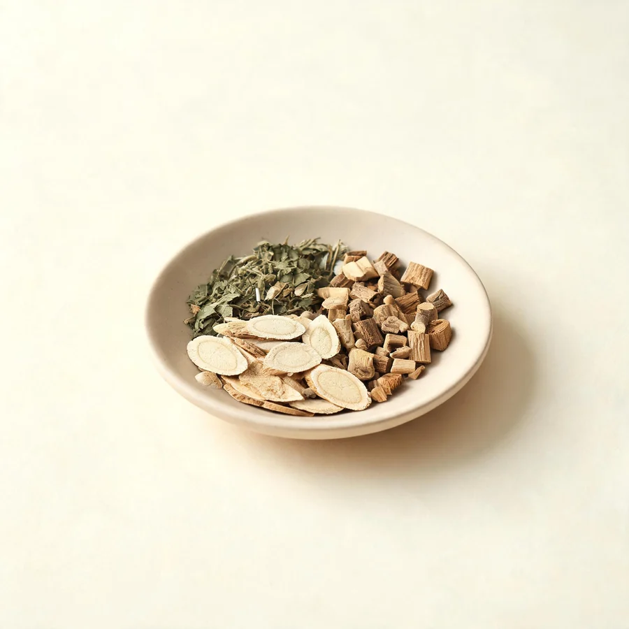 An editorial still life of the traditional Chinese herbs used for this condition, arranged on a warm off-white surface: pale root slices.