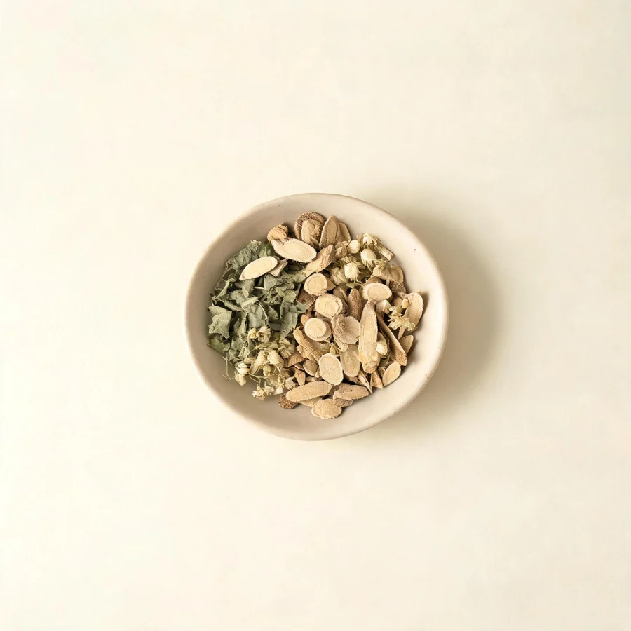An editorial still life of the traditional Chinese herbs used for this condition, arranged on a warm off-white surface: pale root slices.