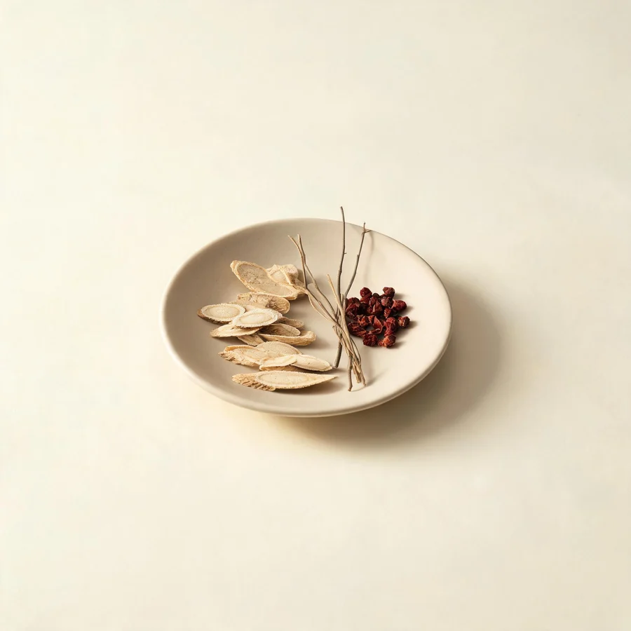 An editorial still life of the traditional Chinese herbs used for this condition, arranged on a warm off-white surface: pale root slices, a.