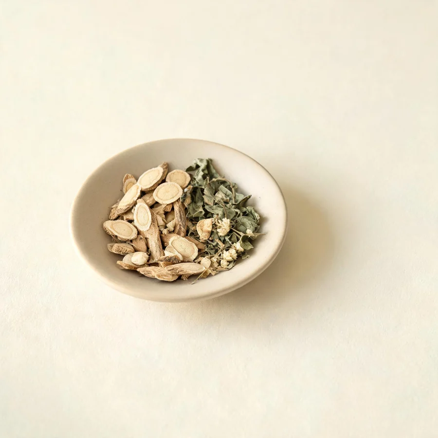 An editorial still life of the traditional Chinese herbs used for this condition, arranged on a warm off-white surface: pale root slices.