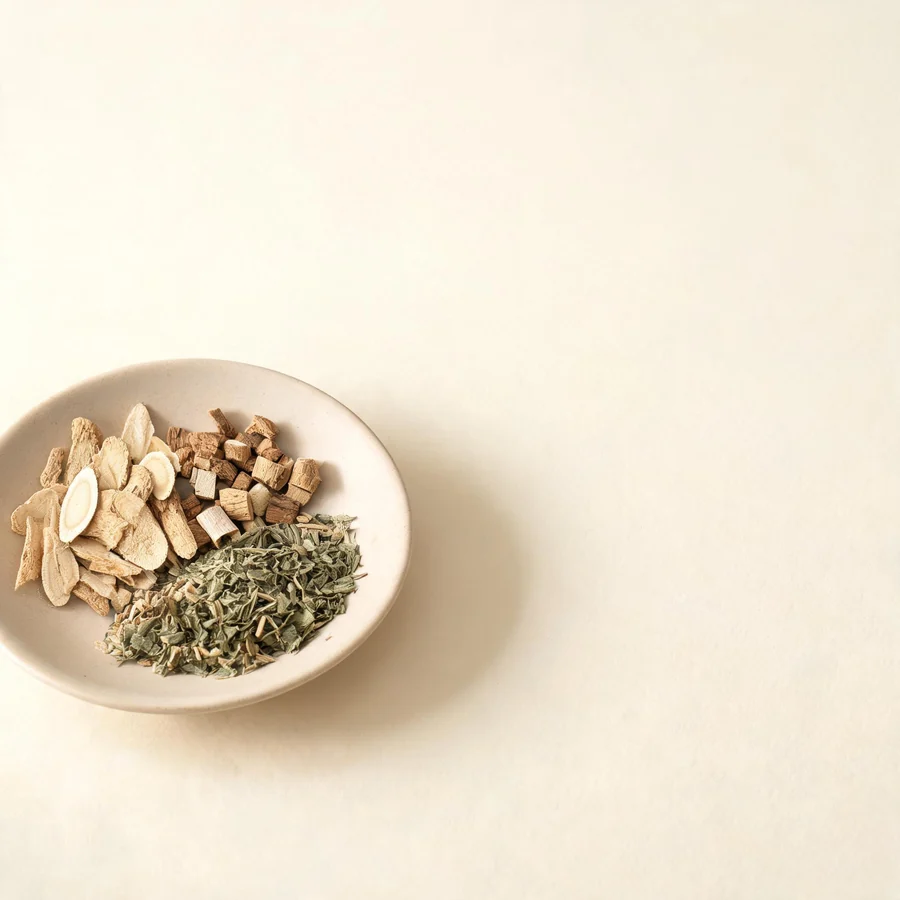 An editorial still life of the traditional Chinese herbs used for this condition, arranged on a warm off-white surface: pale root slices.