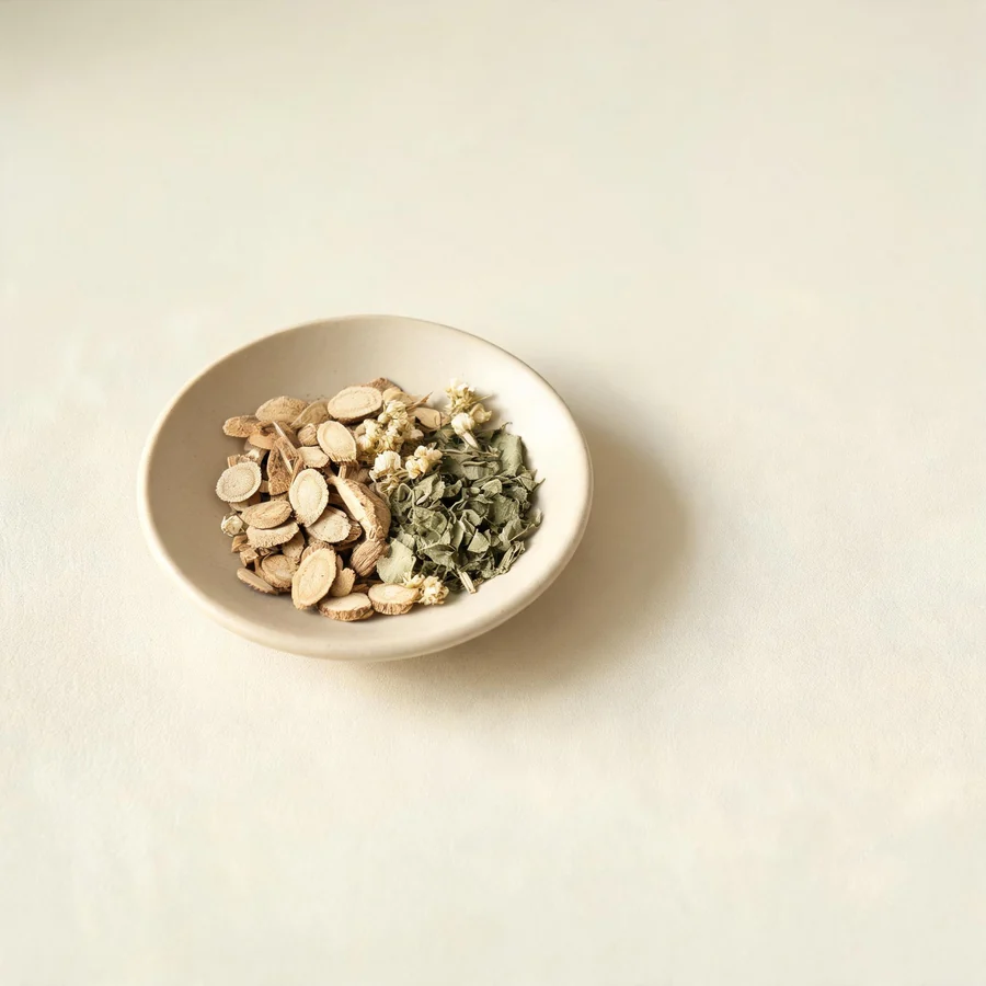 An editorial still life of the traditional Chinese herbs used for this condition, arranged on a warm off-white surface: pale root slices.